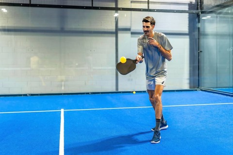 Man playing padel on a vibrant blue court, holding a paddle racket and hitting a bright yellow