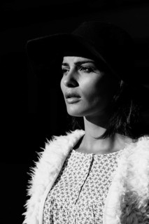 A black and white portrait of a woman in a wide-brimmed hat. The dramatic lighting and shadows