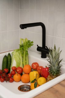 A vibrant assortment of fresh fruits and vegetables in a kitchen sink with a black faucet,