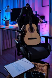 Acoustic guitar on a chair with a microphone in a cozy home studio setting. A notepad with musical