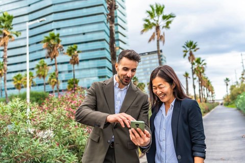 Caucasian businessman and happy asian businesswoman using phone walking along a financial area in
