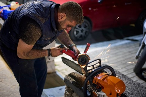 ©Udo Rein, A man uses a grinding machine at night to sharpen the teeth of a chainsaw, Easter fire