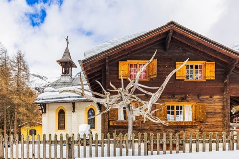 Tree sculpture, behind it an old farmhouse, next to it the Saint Barthélemy chapel, mountain