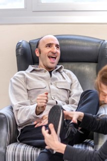 A man laughs joyfully while interacting with a caregiver in a mental health residence. The warm and