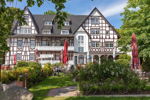 Half-timbered building with outdoor terrace and red parasol in the blooming summer garden, Rügen,