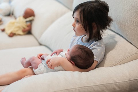 A young girl lovingly holds her newborn sibling on a cozy couch, creating a heartwarming scene of