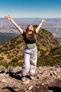 A joyful person with arms outstretched stands on a rocky mountain peak, enjoying panoramic views