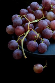 Red grape vine (Vitis vinifera) on plate against dark background