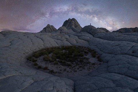 A lone man stands beneath the sprawling Milky Way in the otherworldly terrain of White Pocket,
