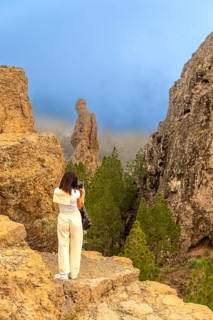 Woman taking pictures of roque nublo, a volcanic rock formation in the mountains of gran canaria,