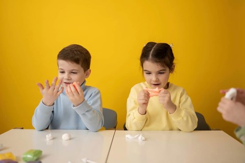 Kids engaged in a creative classroom activity, modeling colorful plasticine. Their expressions of