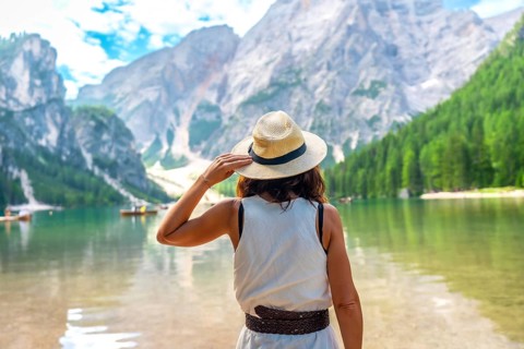 Woman wearing straw hat admiring stunning landscape of lake braies with boats and mountains in