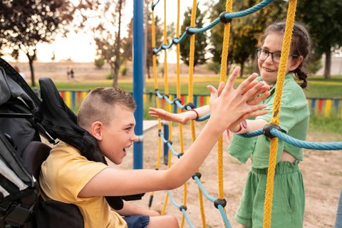 A boy with cerebral palsy and a girl with a tracheostomy enjoy a playful moment on a rope climbing