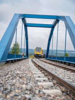 Train runs over rails under blue bridge in scenic surroundings, track construction, rail delivery