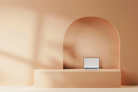 A sleek laptop is placed on a smooth surface against a soft, geometric backdrop. The warm tones