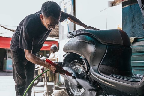 A professional cleaner thoroughly washes a motorcycle using a water hose, focusing on the wheel and