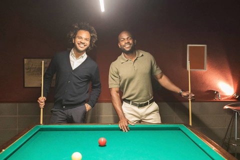 Two smiling men enjoying a game of pool in a relaxed coworking lounge. The welcoming atmosphere