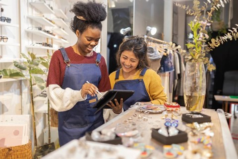 Two employees in a sunglasses store wearing blue aprons are engaging with a digital tablet. They