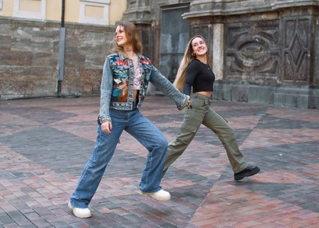 Two young woman friends energetically walk hand in hand across a brick paved area, exuding joy and