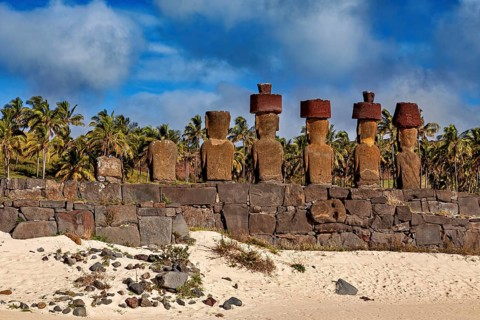 Moai statues on stone wall with a background of palm trees and beach, The Moai statues on Easter