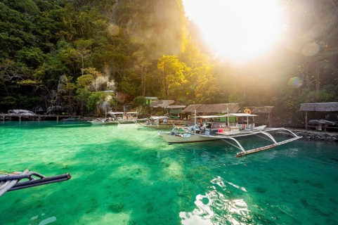 A serene view of a tropical beach in the Philippines showing traditional boats moored in