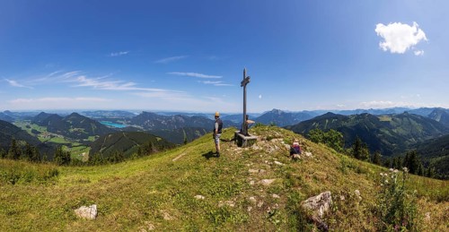 Hikers at the summit cross of the Faistenauer Schafberg with a view of Lake Fuschl, Osterhorn