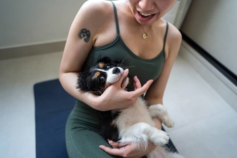 A young woman attempts a home workout while her playful dog interrupts. The scene captures a mix of