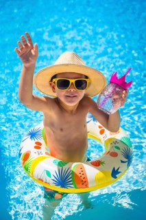 Vertical photo of a caucasian boy playing in a pool inside a rubber ring float while drinking water