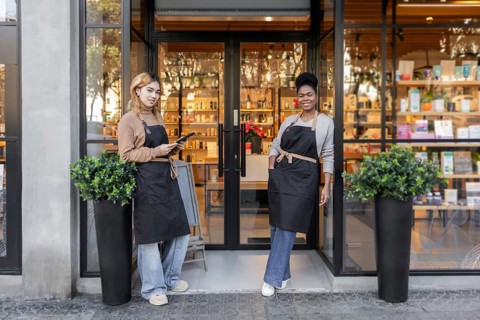 Two employees in aprons stand smiling at the entrance of a chic cosmetics store. The store's