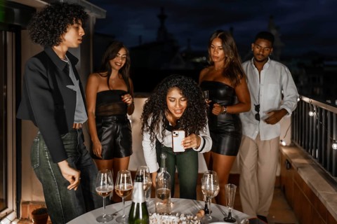 Woman using mobile phone during night party with multi-ethnic friends in a private rooftop with