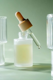 A dropper releasing a single drop of a translucent serum into a matte glass bottle on a serene