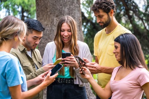 Multiethnic group with phones watching internet or social networks in the park, technology concept