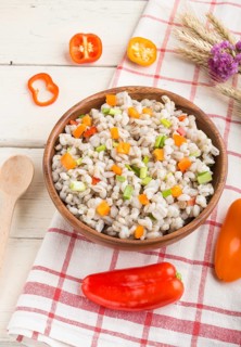 Pearl barley porridge with vegetables in wooden bowl on a white wooden background and linen textile