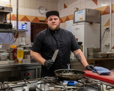 A focused chef in a professional kitchen setting, holding a knife with confidence. The kitchen is