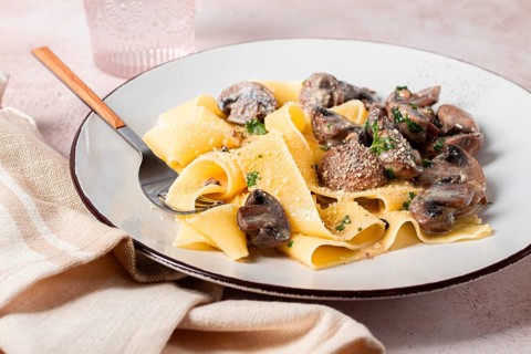Delicious pappardelle pasta with mushrooms and cream served on a white plate