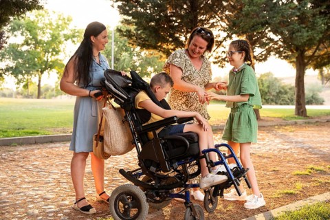A family enjoys time together in a park, featuring a disabled girl with a tracheostomy and a boy