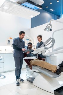 Dentist and dental nurse showing information on a digital tablet to a patient lying on a dentist