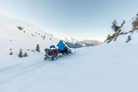 A snowmobiler in a blue jacket speeds through pristine snow-covered mountains, capturing the thrill