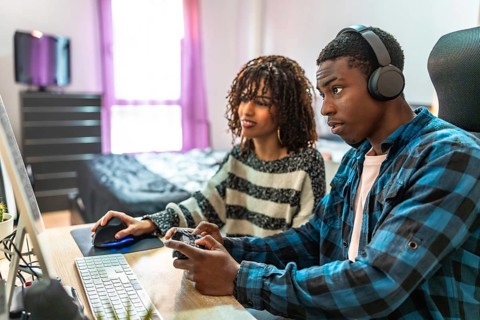 Young man and woman enjoying their time together, playing video games on a computer and gamepad