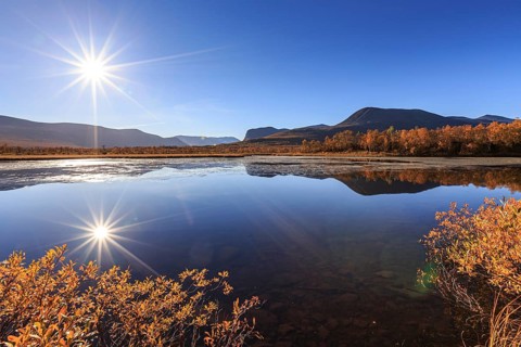 Mountains reflected in lake, autumn colours, sun, sun star, bright, friendly, Nikkaluokta, Laponia,