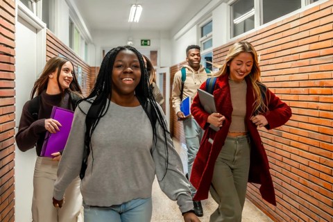 Cheerful multi ethnic university students walking together in a bustling school corridor, sharing