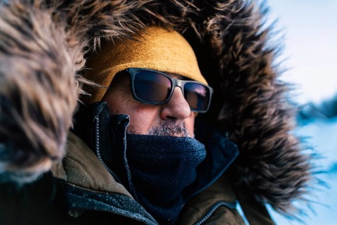 An adventurer warmly dressed in a fur-lined hood and sunglasses faces the harsh yet beautiful