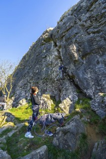 Two female rock climbers ascending a challenging rock face in nature, one belaying from below while