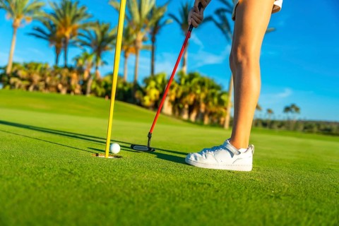 Unrecognizable female young golfer putting golf ball on the green golf