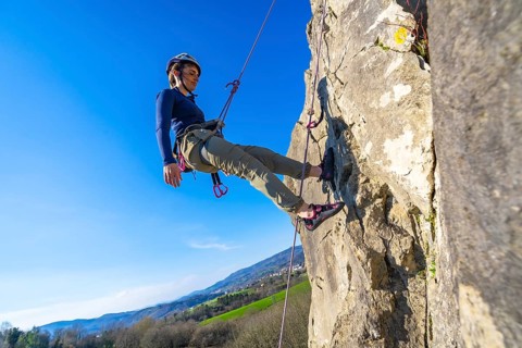 Young woman climber ascending a steep rock face using ropes and climbing gear, enjoying a sunny day
