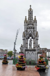 Large stone monument with colourful flowers in a town square, Cork