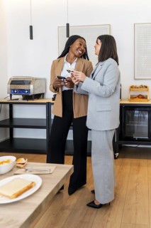 Two smiling businesswomen using a smartphone and credit card, enjoying breakfast during their