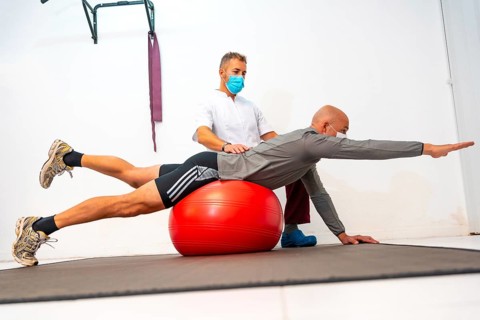 Physiotherapist with face mask helping client to balance on a red ball. Physiotherapy with