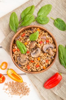 Spelt (dinkel wheat) porridge with vegetables and mushrooms in wooden bowl on a white wooden