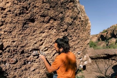 A climber tackles a rugged boulder, demonstrating skill and focus in a natural setting. The sunlit